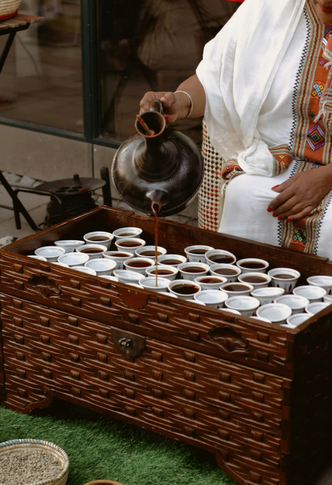 Coffee poured from a black clay jebena into rows of small white cups during an Ethiopian coffee ceremony